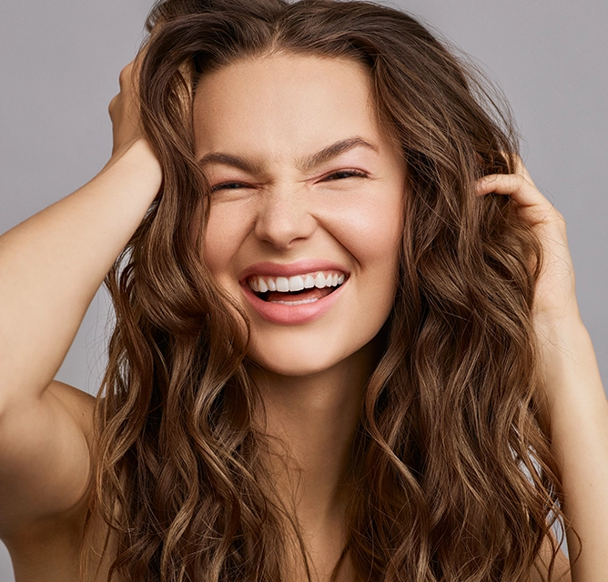 Smiling woman running both hands through her wavy brown hair