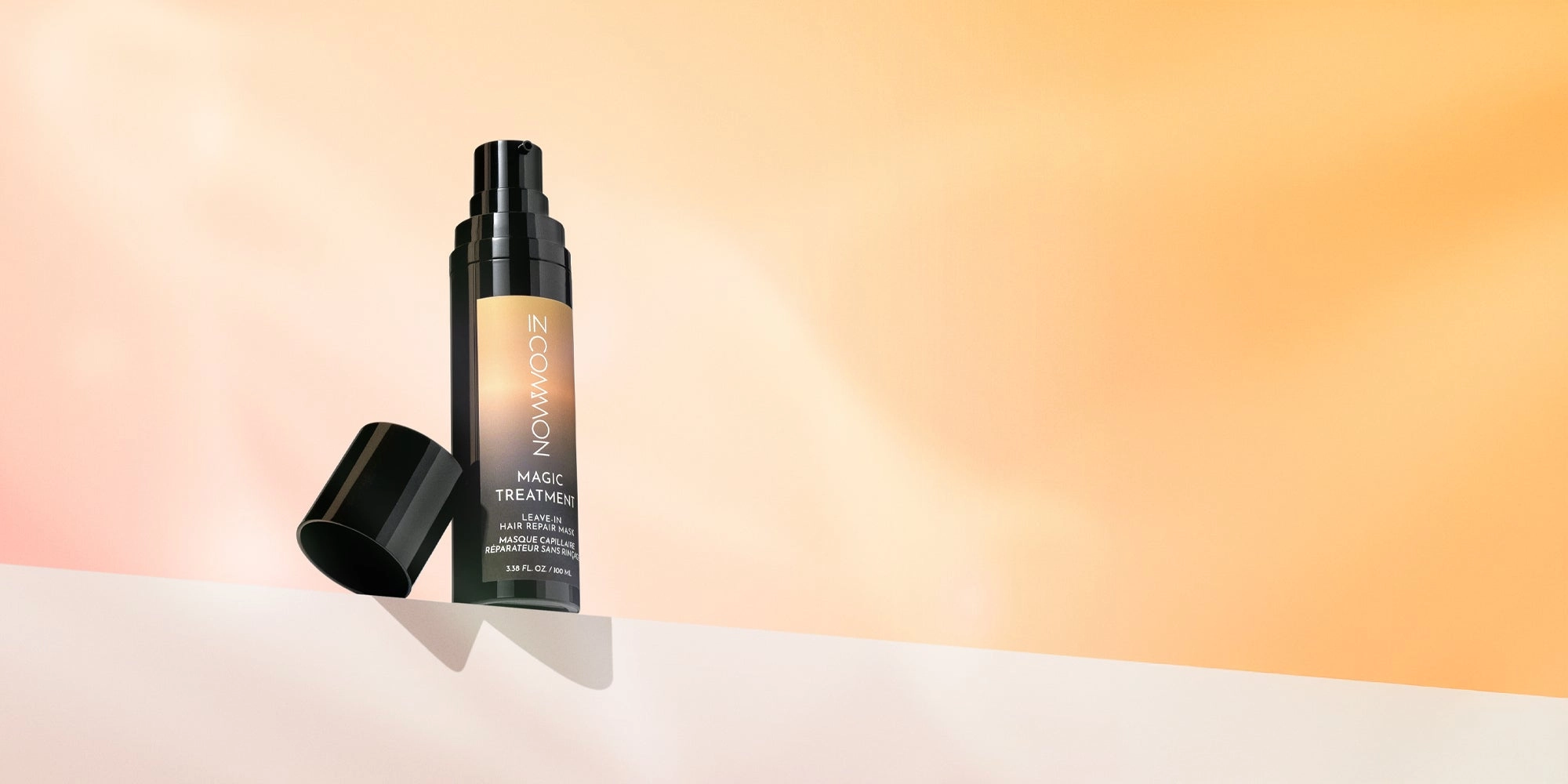 Magic Treatment leave-in hair repair mask bottle standing on a pale ledge against a peach backdrop