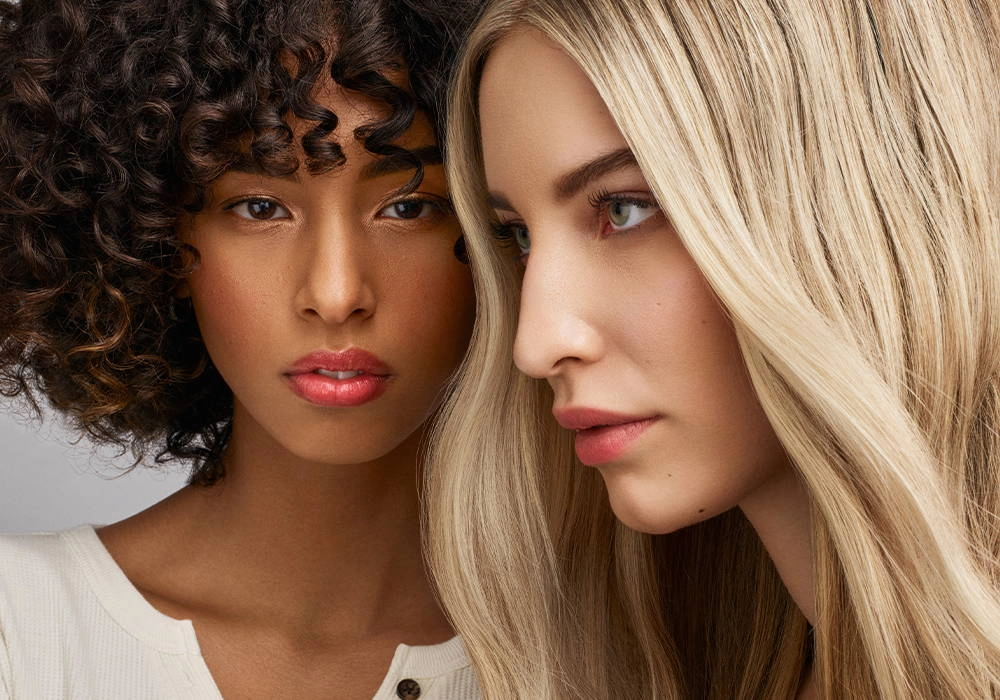 Two women with curly and blonde hair, faces close together