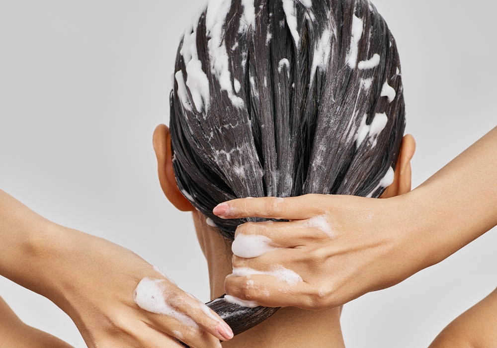 Hands working a foamy treatment through long hair